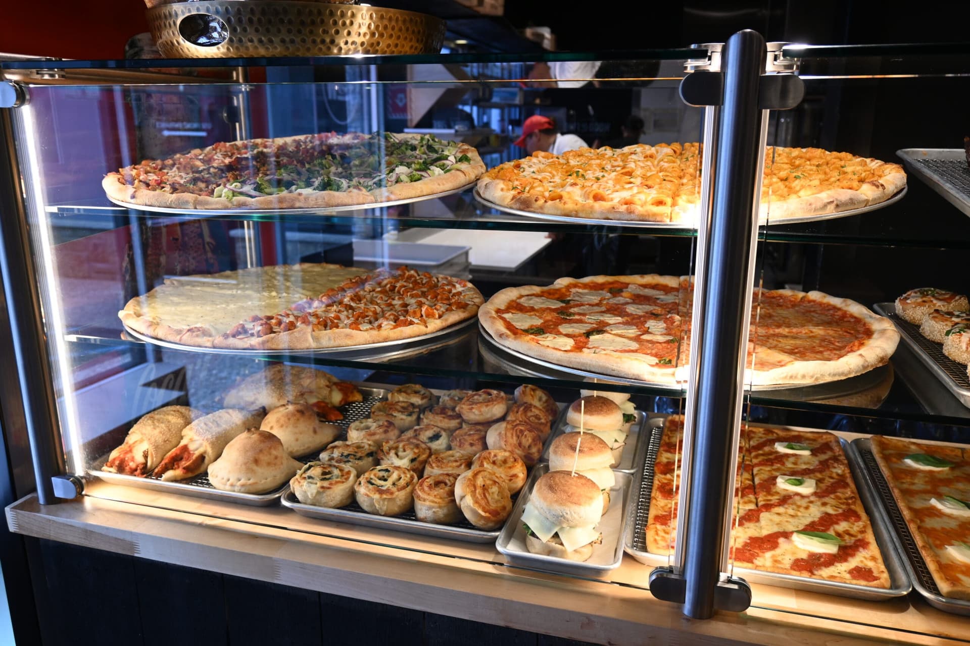 The display case at the counter, filled with whole pies, slices, calzones and rolls