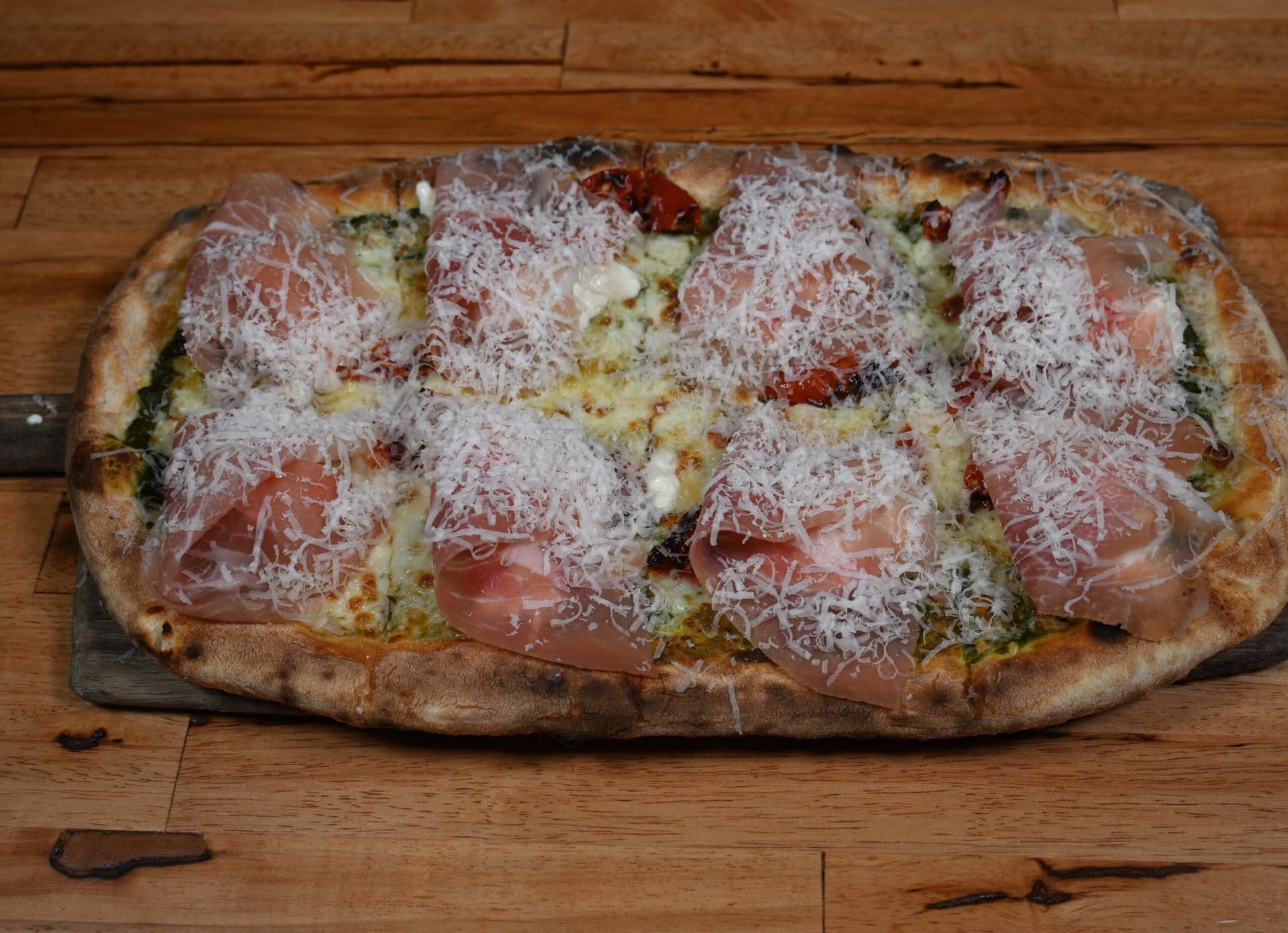 A fig and prosciutto pizza on a wooden board, blistered crust, shaved parmigiano
